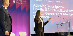 two people onstage in front of a screen that reads “Achieving fusion ignition: how the U.S. national labs power the next generation of advanced technologies”
